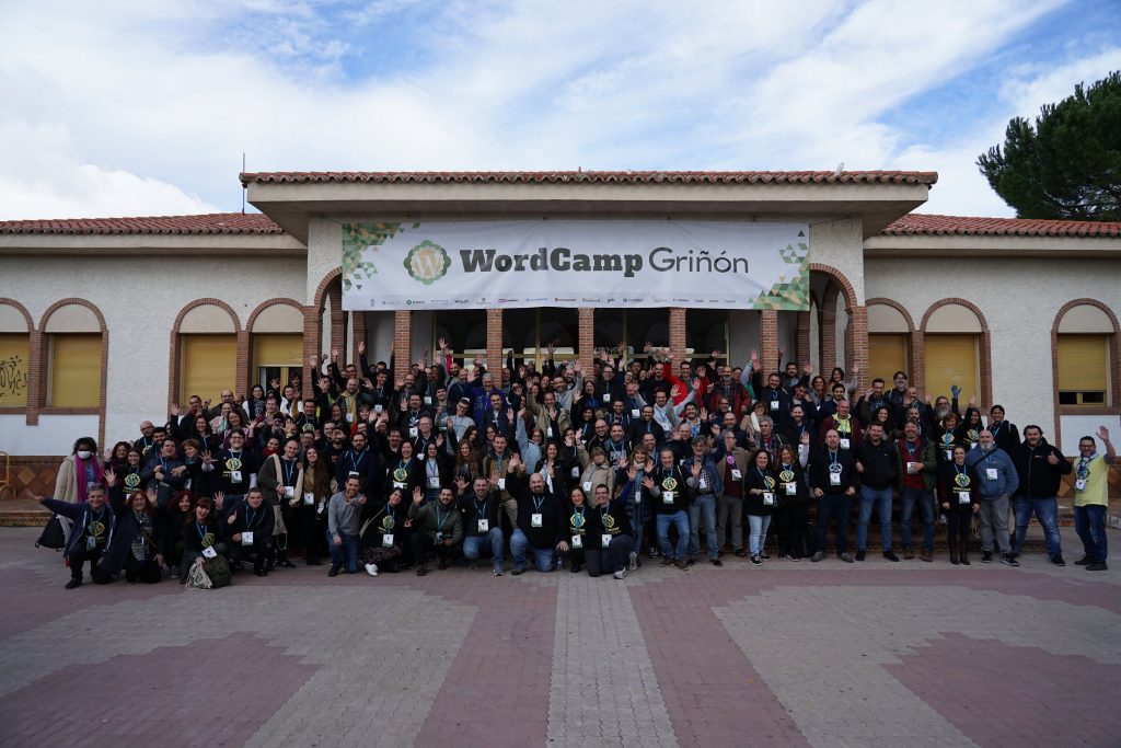 Foto de todos los asistentes de WordCamp Griñón 2022 delante del Centro Cultural de Griñón. Con una lona horizontal que pone WordCamp Griñón.